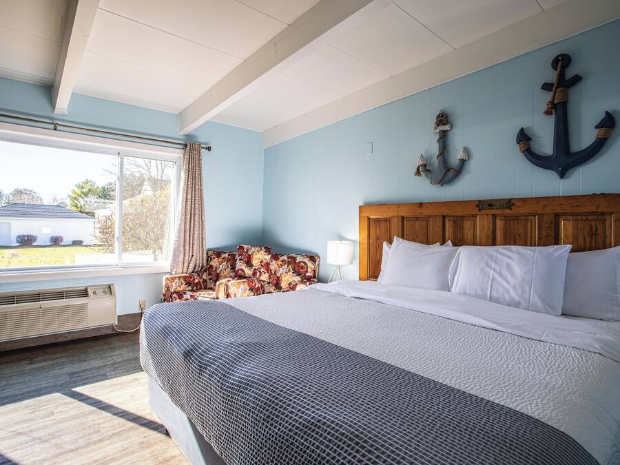 A bedroom with a large bed, a wooden headboard, a window with curtains, and two anchors on the wall.