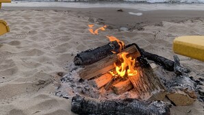 Une plage avec un foyer au milieu du sable, entourée de chaises jaunes.