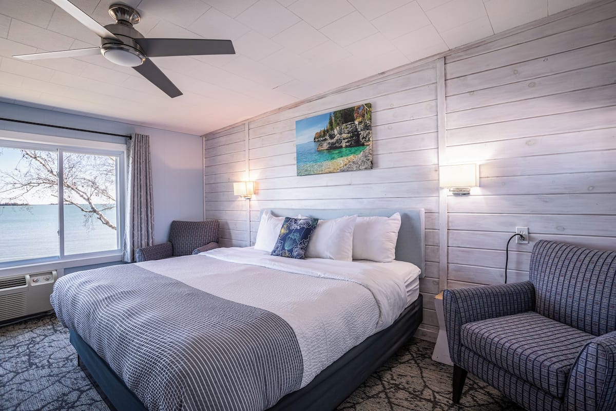A hotel room with a large bed, a ceiling fan, a view of the sea, and a painting on the wall.