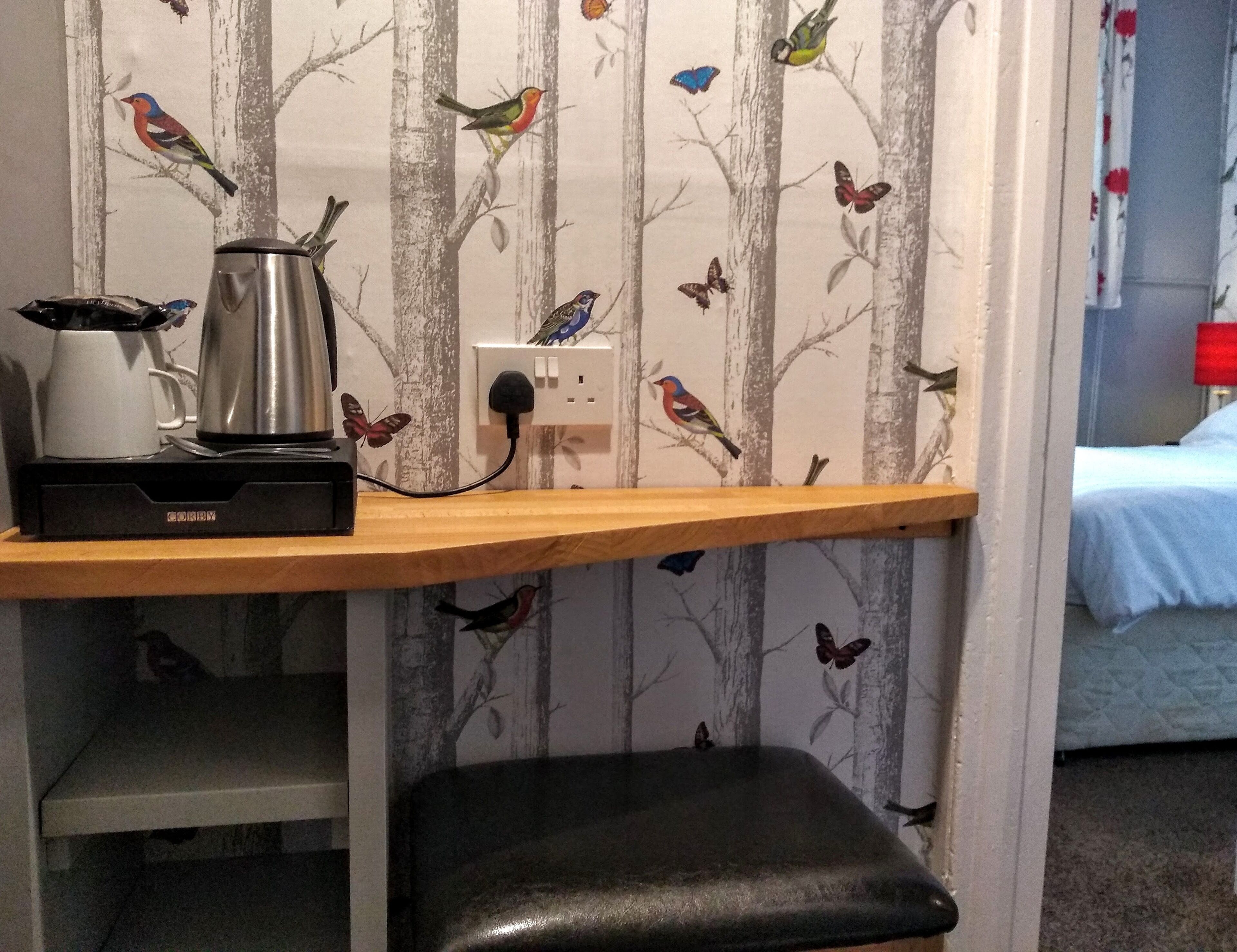 A small room with a wooden shelf holding a kettle and a power outlet.