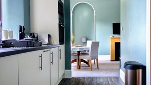 A modern kitchen with white cabinets, a black countertop, and a dining area with a table and chairs. - Bluebird Lodge and Waterhead Apartment (Coniston)