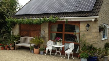 A house with a solar panel roof, a wooden door, and a garden with potted plants and outdoor furniture.