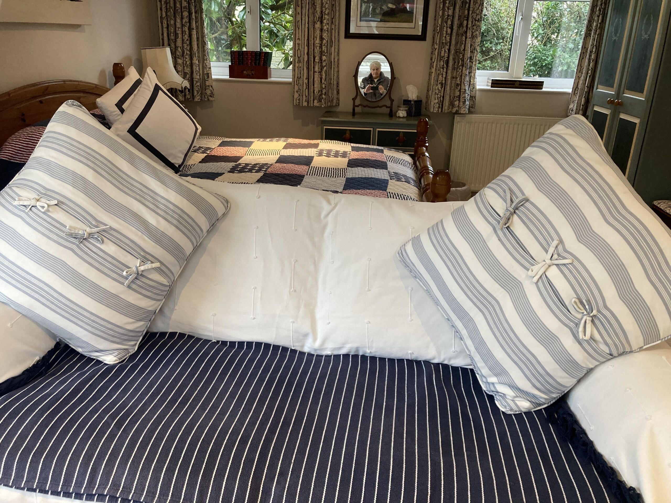 A bed with striped bedding and a quilt, a dresser with a mirror, and a window with curtains.