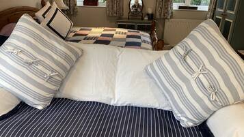 A bed with striped bedding and a quilt, a dresser with a mirror, and a window with curtains.
