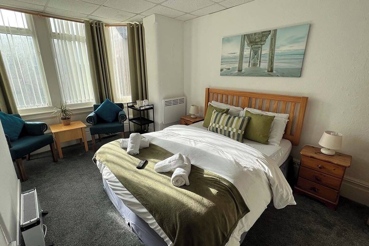 A hotel room with a bed, a desk, a chair, a lamp, and a painting on the wall.
