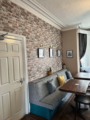 Una habitación acogedora con pared de ladrillo, una puerta blanca, un detalle azul en el sofá y una mesa de comedor con sillas.
