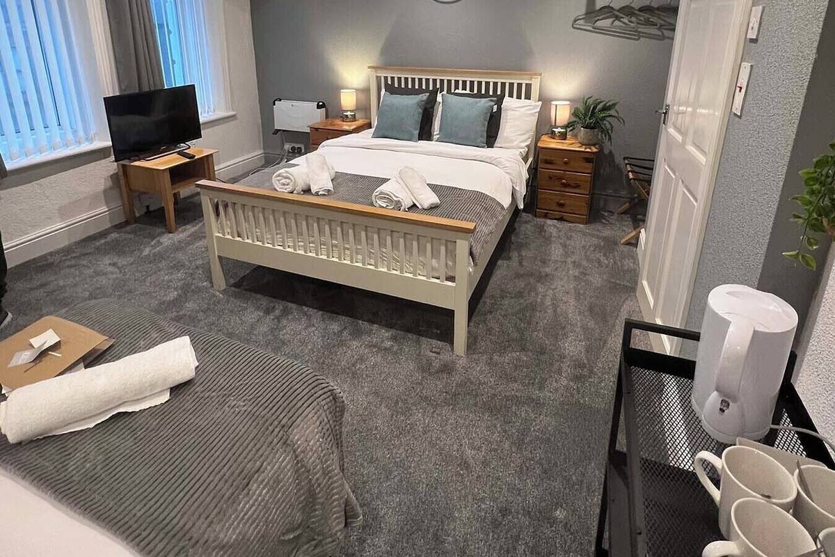A modern hotel room with a large bed, bedside tables, a TV, and a small seating area.