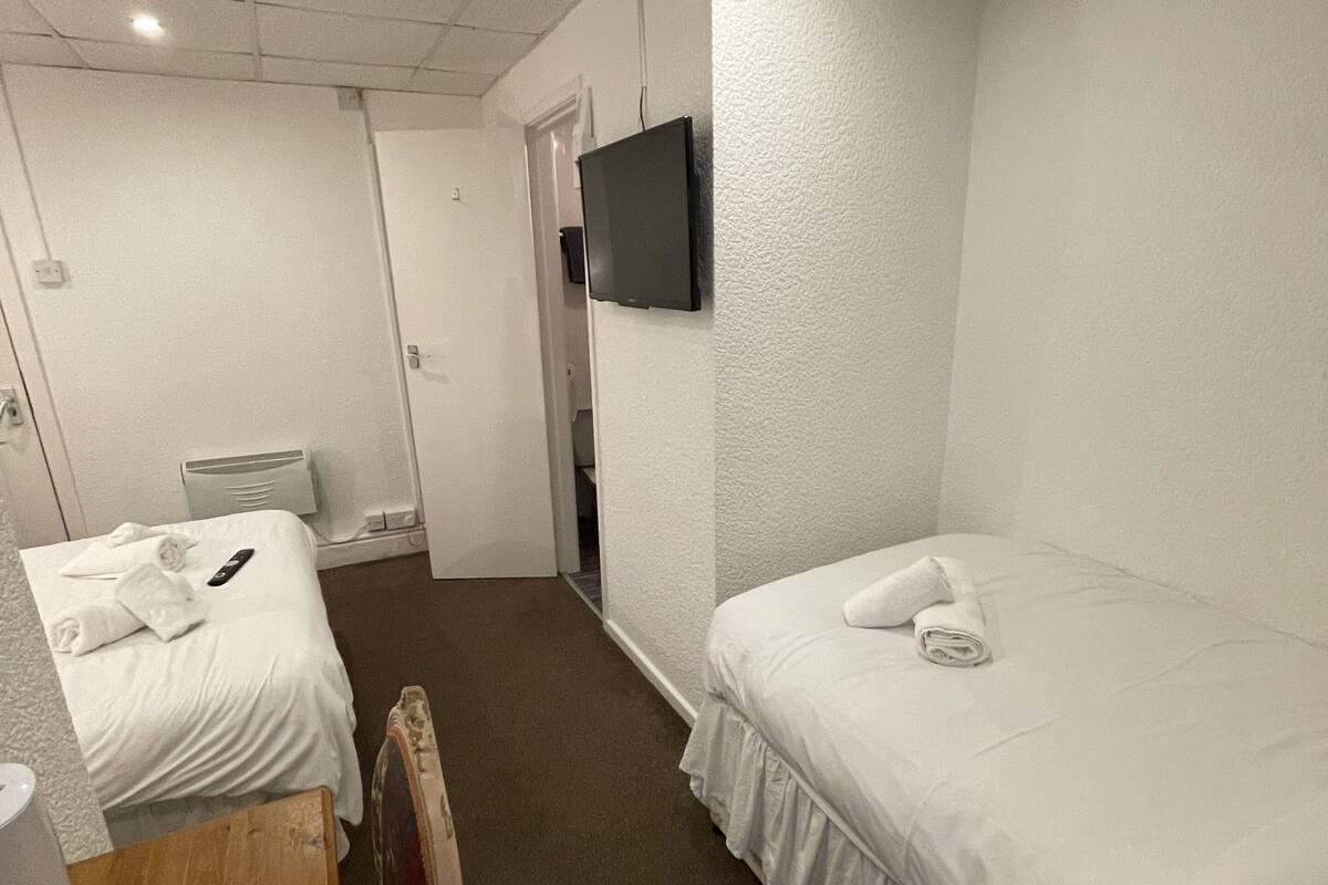 A hotel room with two single beds, a wooden table, a TV mounted on the wall, and a small seating area.