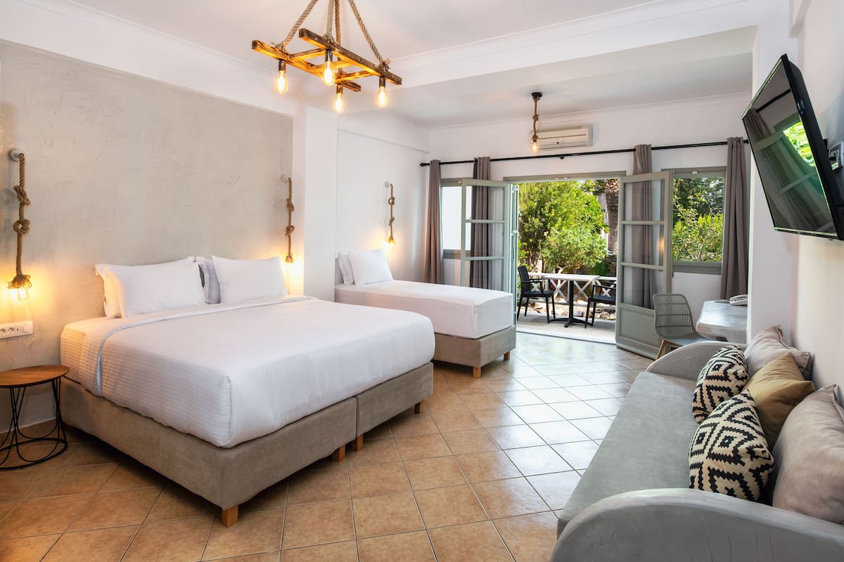 A bedroom with two beds, a sofa, a TV, and a balcony with a table and chairs.