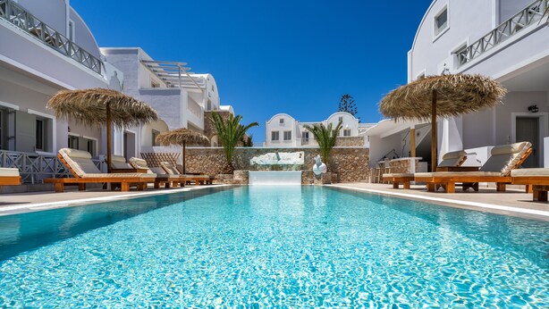 A pool with lounge chairs and umbrellas, surrounded by white buildings with balconies. - Kalya Suites (Santorini)