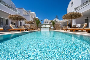 A pool with lounge chairs and umbrellas, surrounded by white buildings with balconies. - Kalya Suites (Santorini)