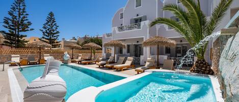A swimming pool with lounge chairs, a decorative vase, and a waterfall feature.