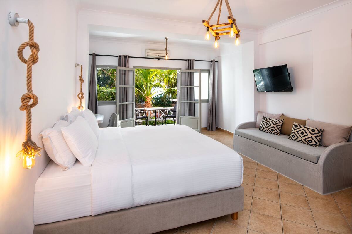 A bedroom with a bed, a sofa, a TV, and a view of the outdoors.