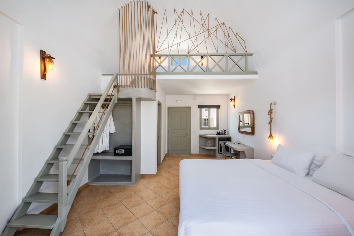 A bedroom with a large bed, a desk, a chair, a wardrobe, and a staircase.