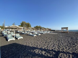 På stranden, sort sand, solsenger og parasoller