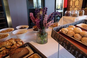 A buffet table with various food items, including croissants, bread, and pastries, along with a vase of flowers. - Aiguille Grive Chalets Hôtel (Bourg-Saint-Maurice)