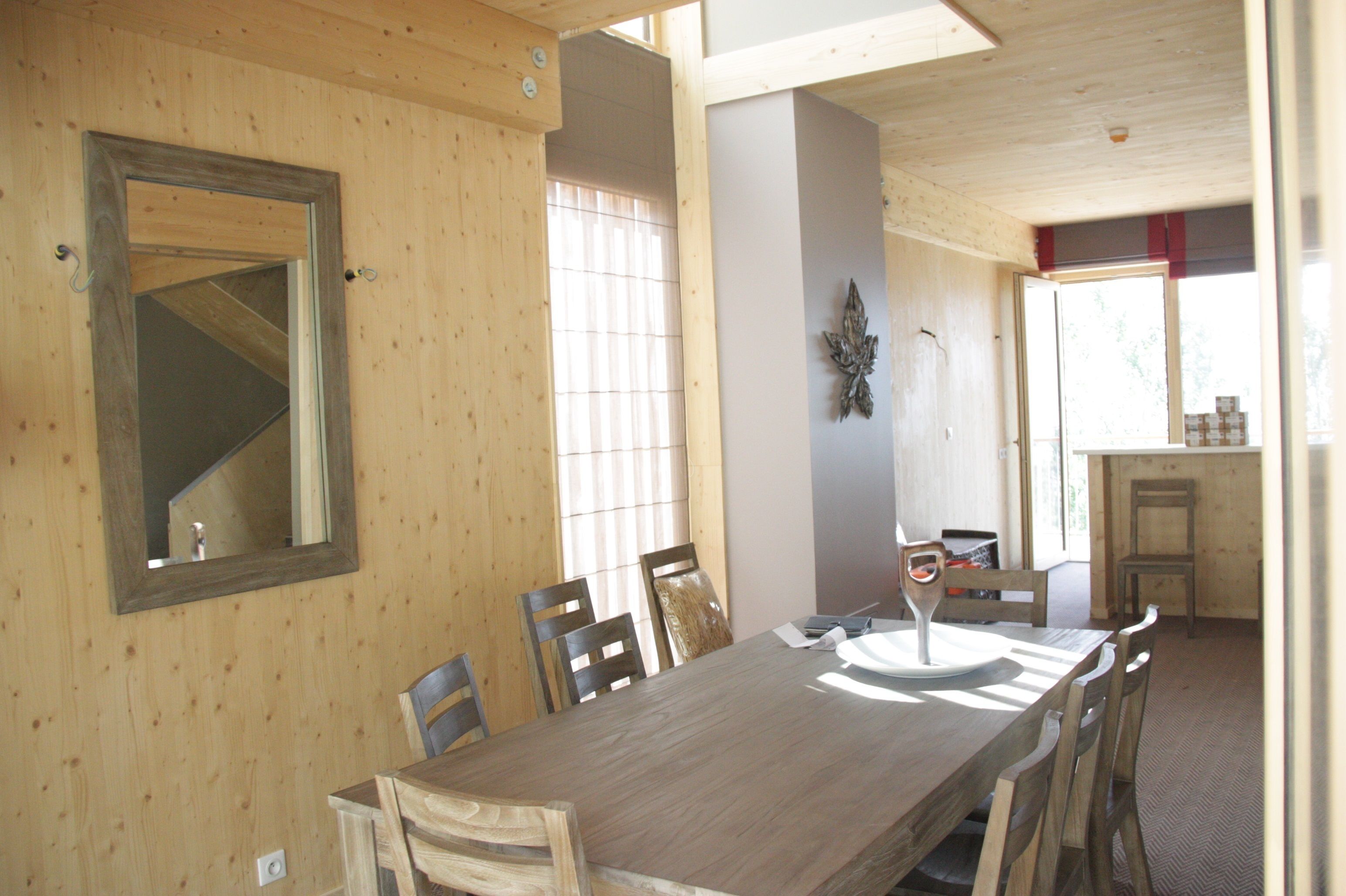 A wooden dining room with a large table and chairs, a mirror on the wall, and a window with blinds.