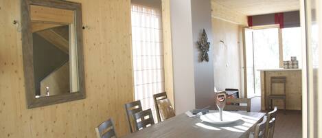 A wooden dining room with a large table and chairs, a mirror on the wall, and a window with blinds.