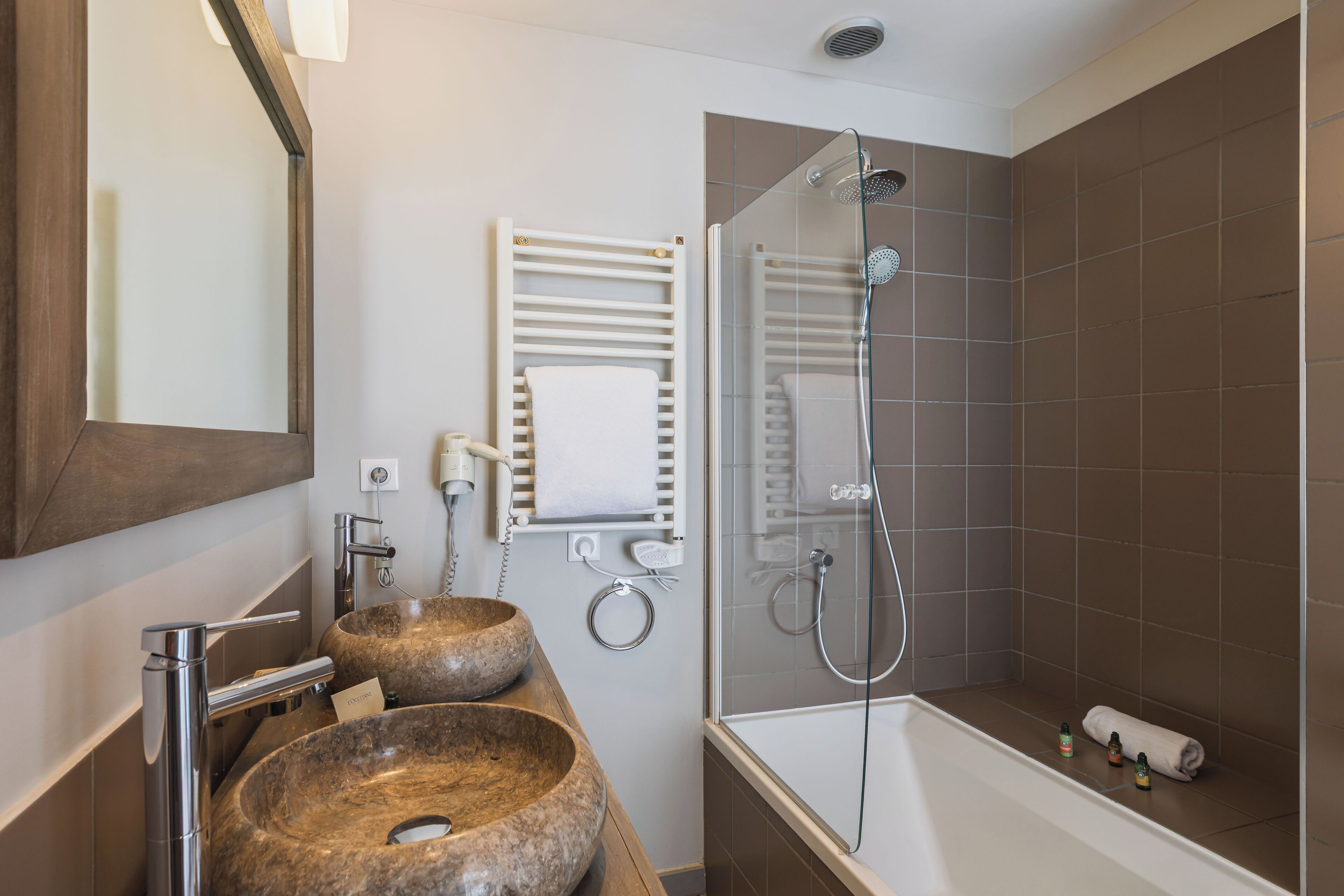 Een moderne badkamer met twee stenen wastafels, een douche met glazen wand en een witte handdoekhouder.