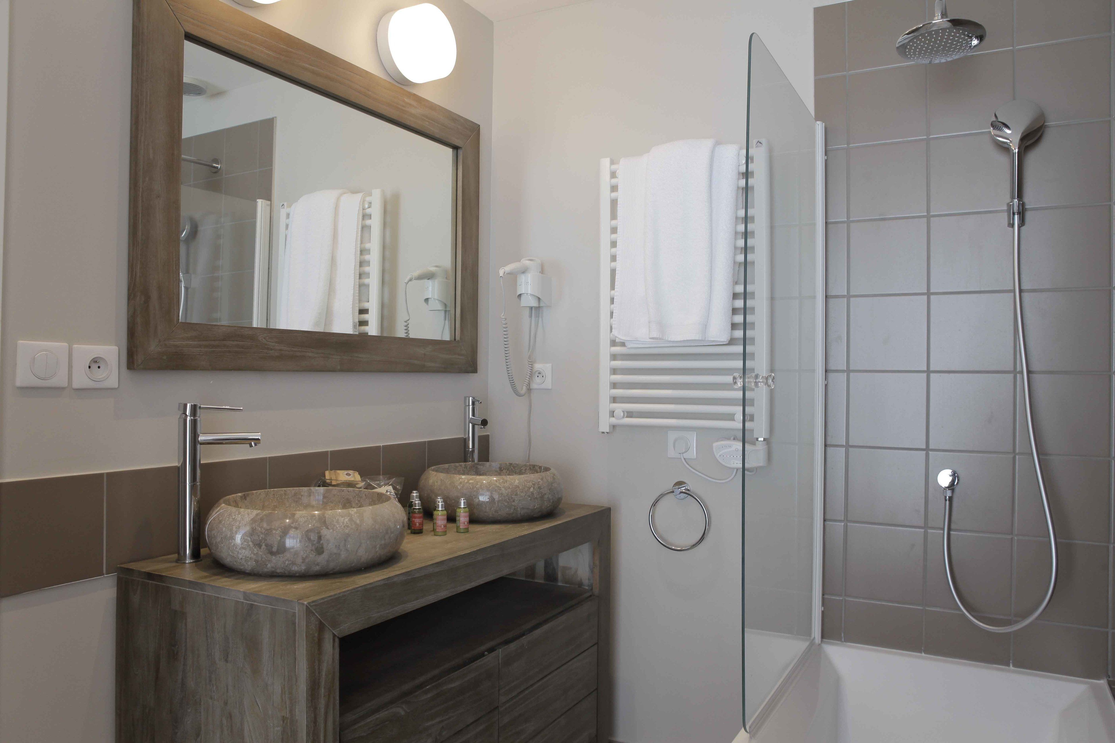 Een badkamer met een houten wastafelmeubel, twee wasbakken, een grote spiegel, een douche en een handdoekrek.
