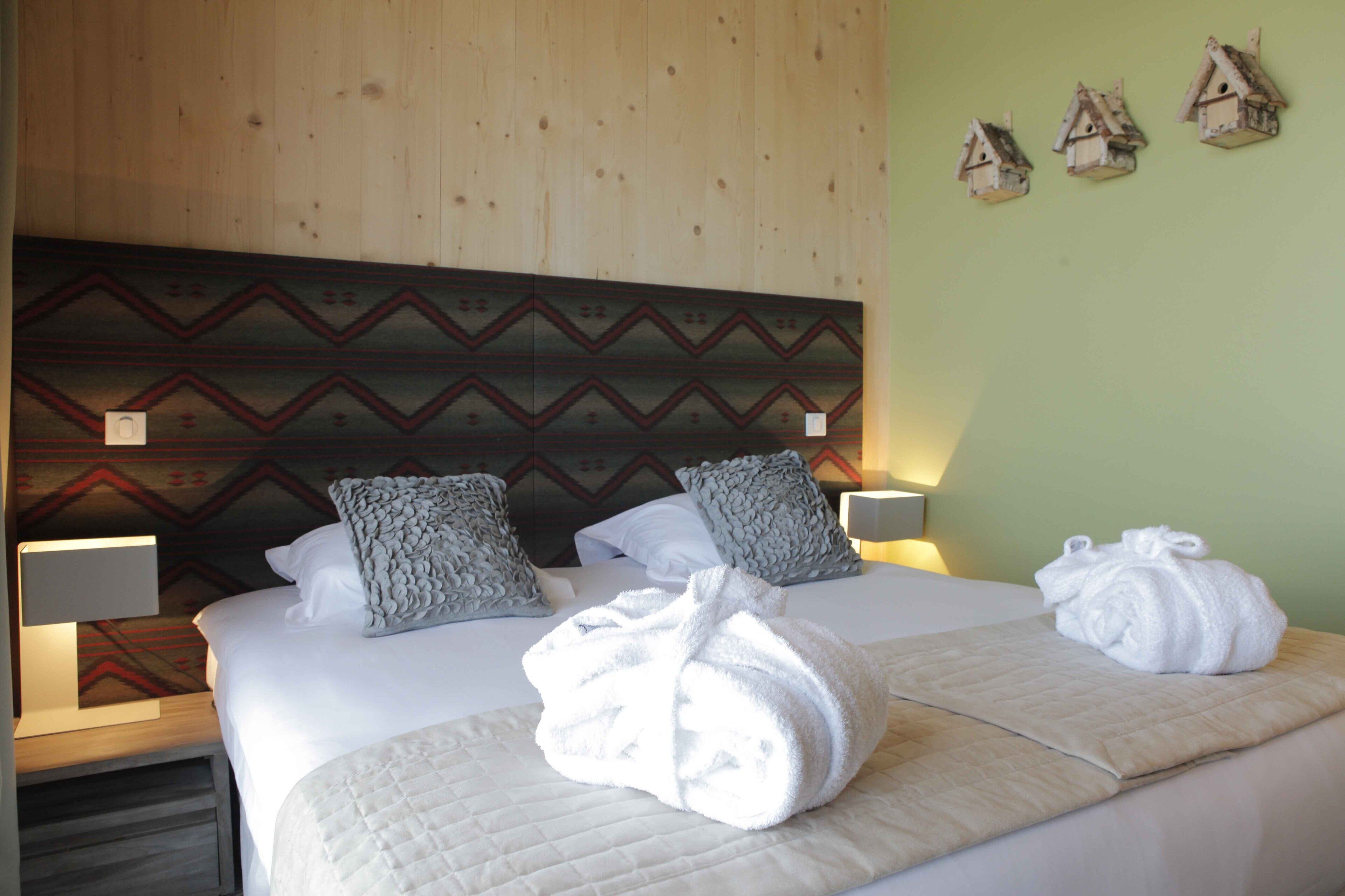 A hotel room with a bed, two pillows, a blanket, and a towel.