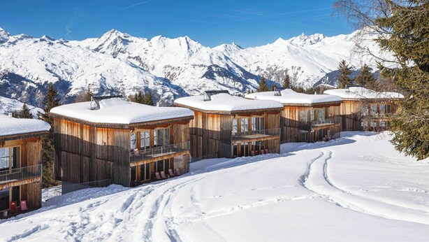 A row of wooden cabins with snow-covered roofs, set against a backdrop of snow-capped mountains. - Aiguille Grive Chalets Hôtel (Bourg-Saint-Maurice)