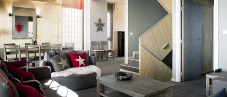 A modern living room with a wooden ceiling, a dining area with chairs, and a staircase leading to another level.