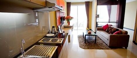 A modern kitchen with a sink, stove, and cabinets. There is a dining area with a table and chairs, and a living room with a sofa and a coffee table.