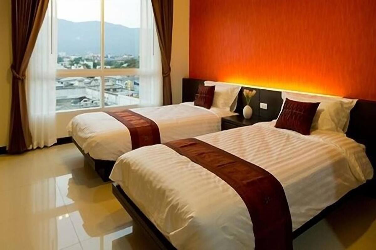 A hotel room with two beds, a large window with a view, and a red accent wall.