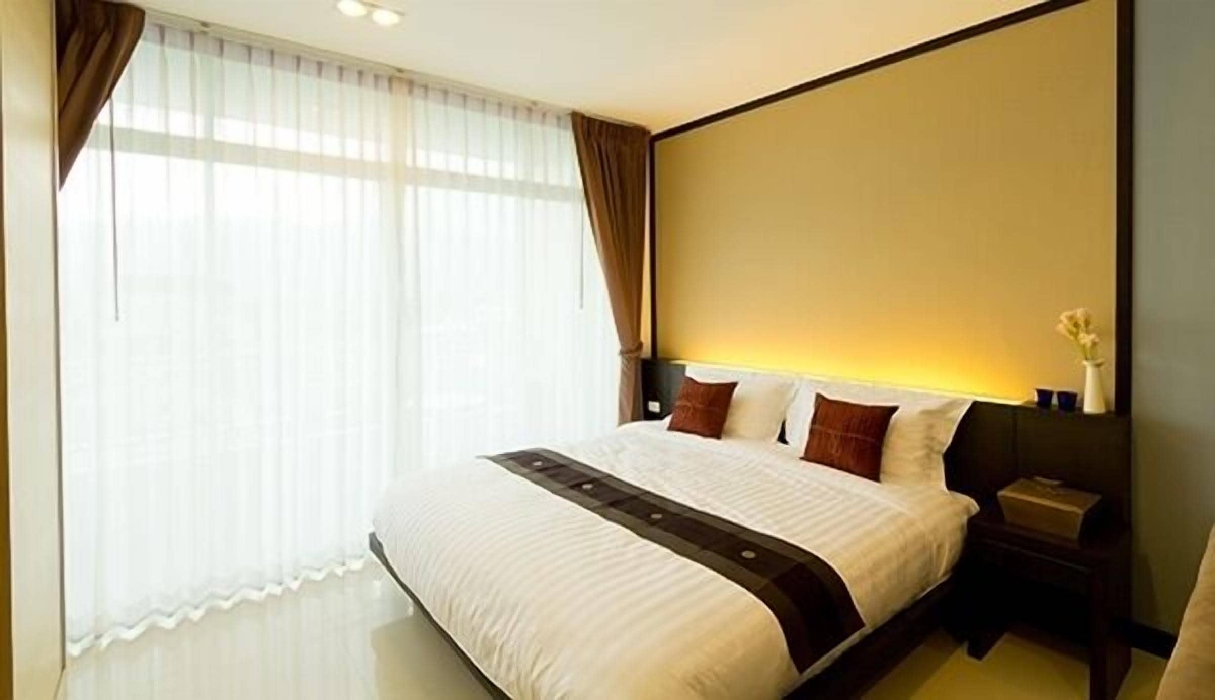A hotel room with a large bed, a nightstand, a vase with flowers, and a window with curtains.