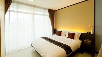 A hotel room with a large bed, a nightstand, a vase with flowers, and a window with curtains.