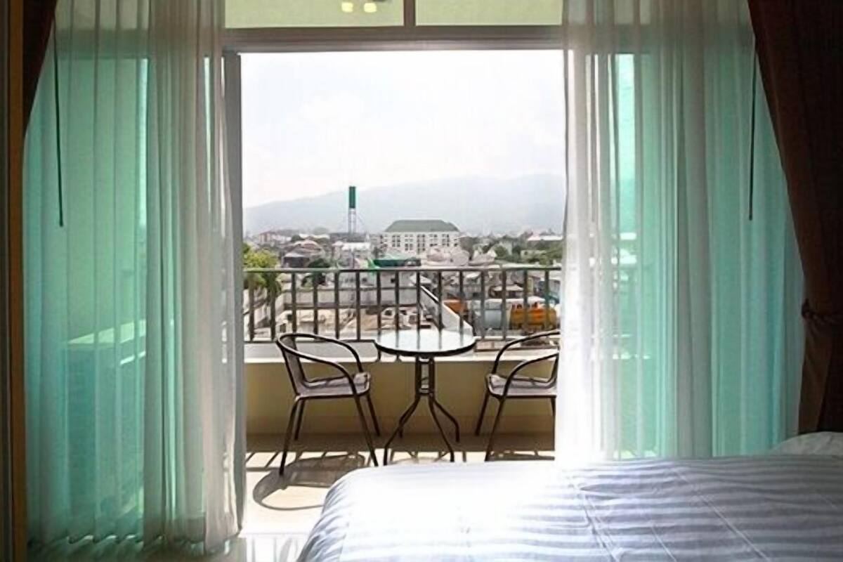 A hotel room with a balcony featuring a table and chairs, a bed, and a view of the cityscape.
