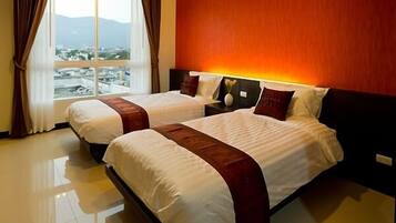 A hotel room with two beds, a large window with a view of a cityscape, and a red accent wall.