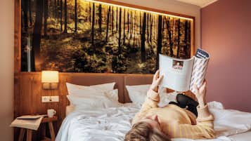 Eine Person liegt im Bett und liest ein Buch in einem Raum mit einer großen Waldmalerei an der Wand.