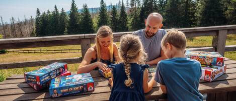 Una familia de cuatro personas en una mesa de picnic de madera, con juegos de mesa y una caja de pizza.
