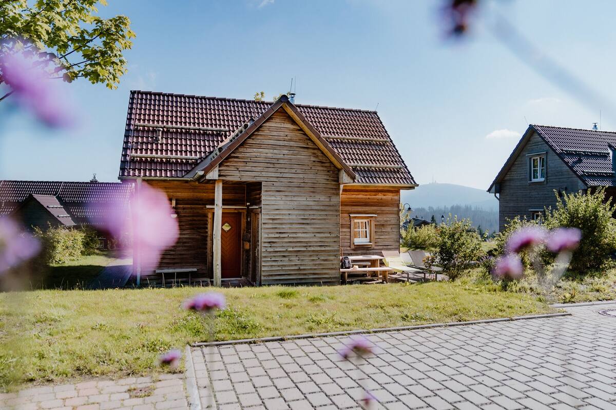 A wooden cabin with a tiled roof, a wooden door, and a small porch with a bench.
