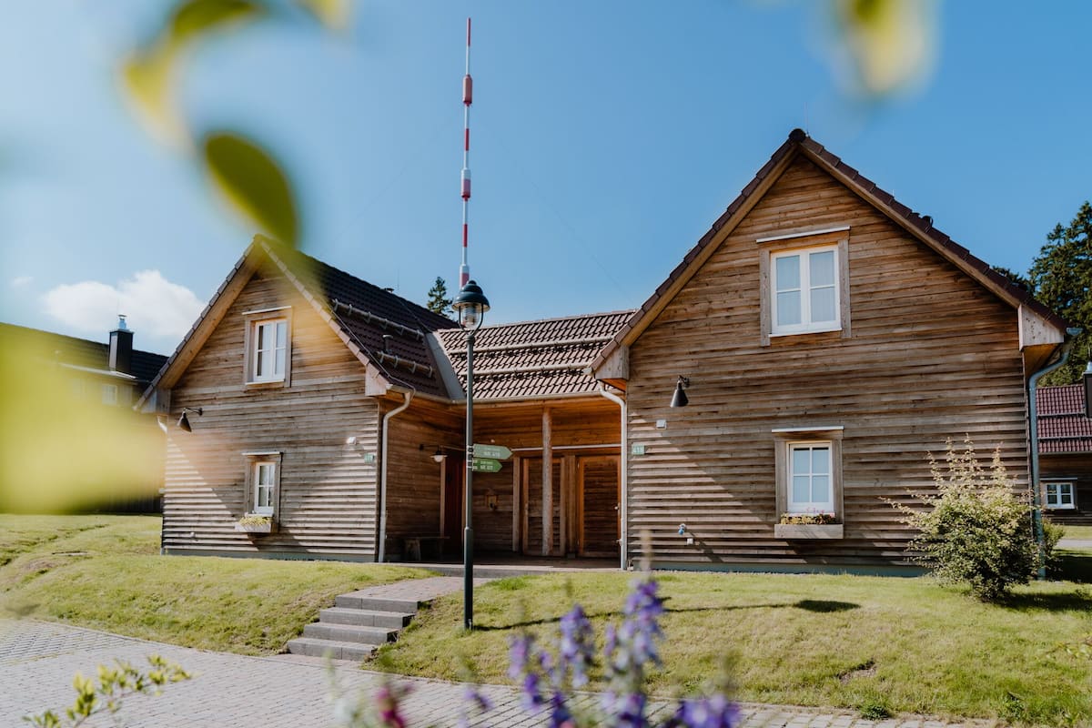 A wooden house with a sloped roof, a small porch, and a flagpole.