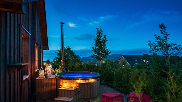 A wooden deck with a hot tub, outdoor lighting, and a view of the mountains. - Torfhaus HARZRESORT (Clausthal-Zellerfeld)