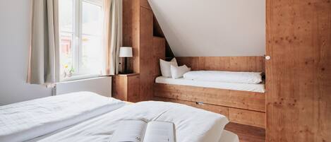 Een slaapkamer met twee bedden, een houten hoofdbord, een raam met gordijnen en een lamp op een nachtkastje.