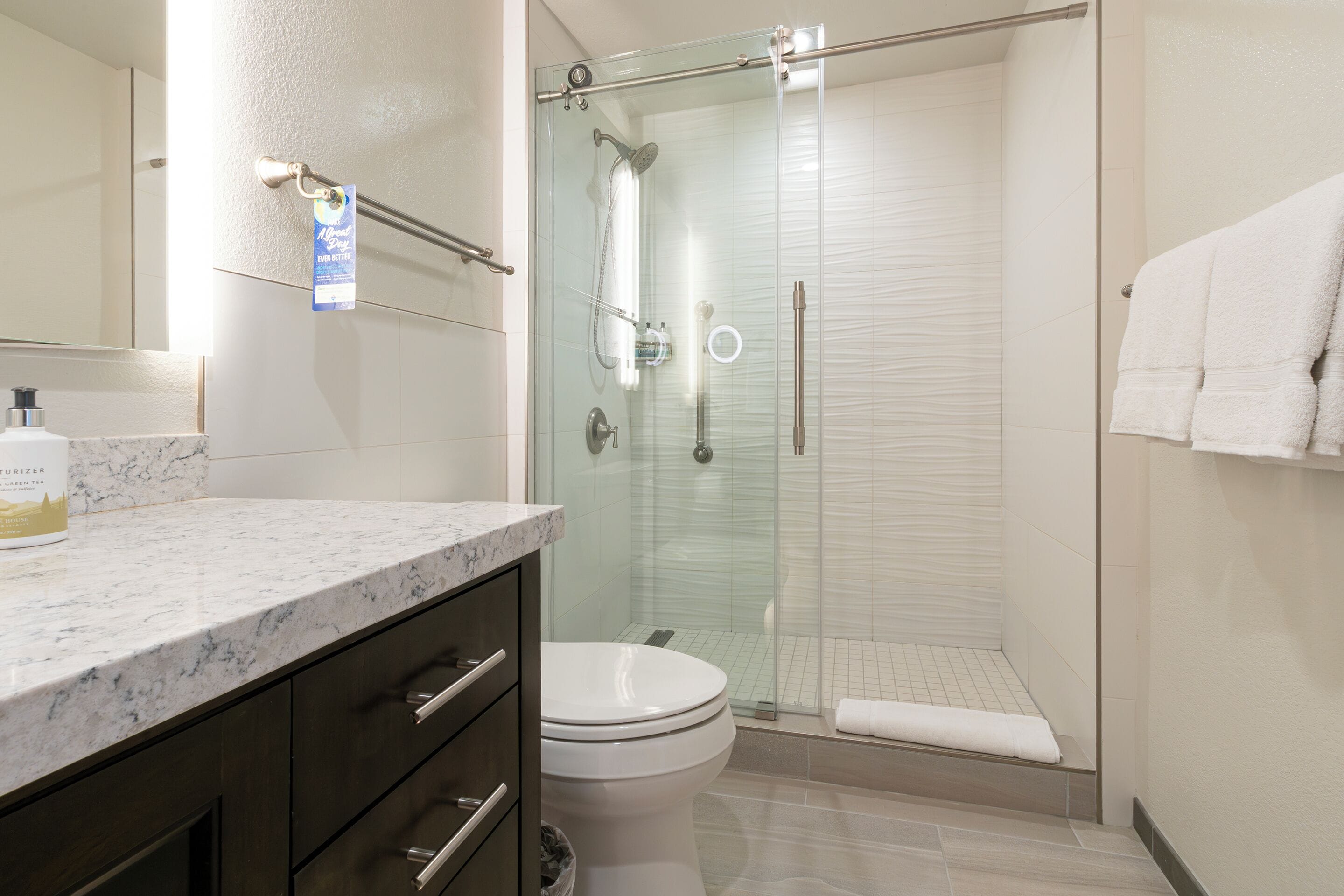 A modern bathroom with a glass-enclosed shower, a toilet, and a marble countertop.