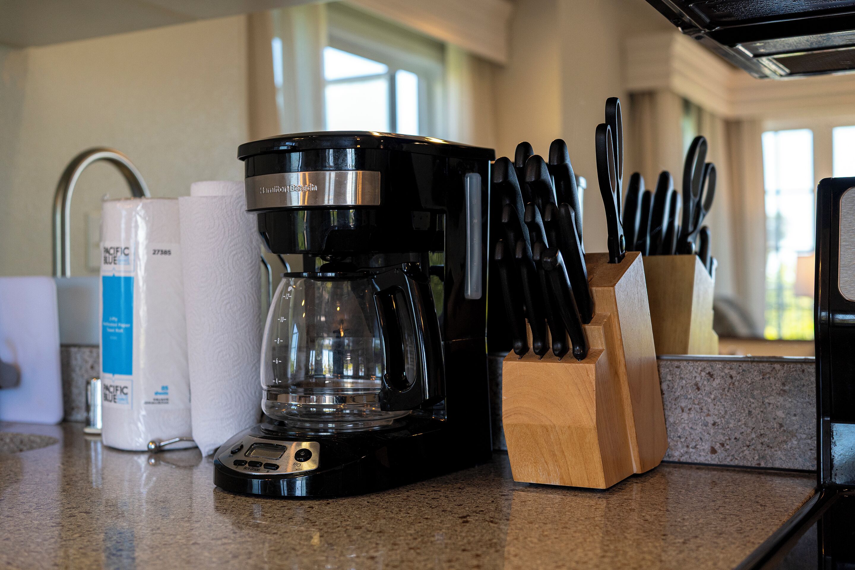 A coffee maker, paper towels, and a knife block on a kitchen counter.