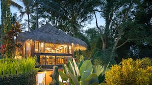 A thatched-roof structure with a glass facade, surrounded by lush greenery. - Villa Kupu-Kupu (Ubud)