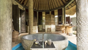 A traditional bath area with a large stone basin, a wooden stool, and a thatched roof structure. - Villa Kupu-Kupu (Ubud)