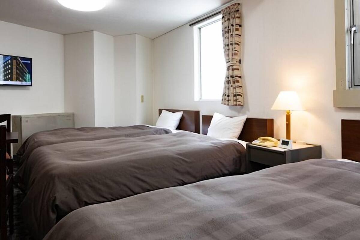 Ein Hotelzimmer mit zwei Betten, einem Schreibtisch, einem Sessel, einer Lampe, einem Telefon und einem Fenster mit Vorhängen.