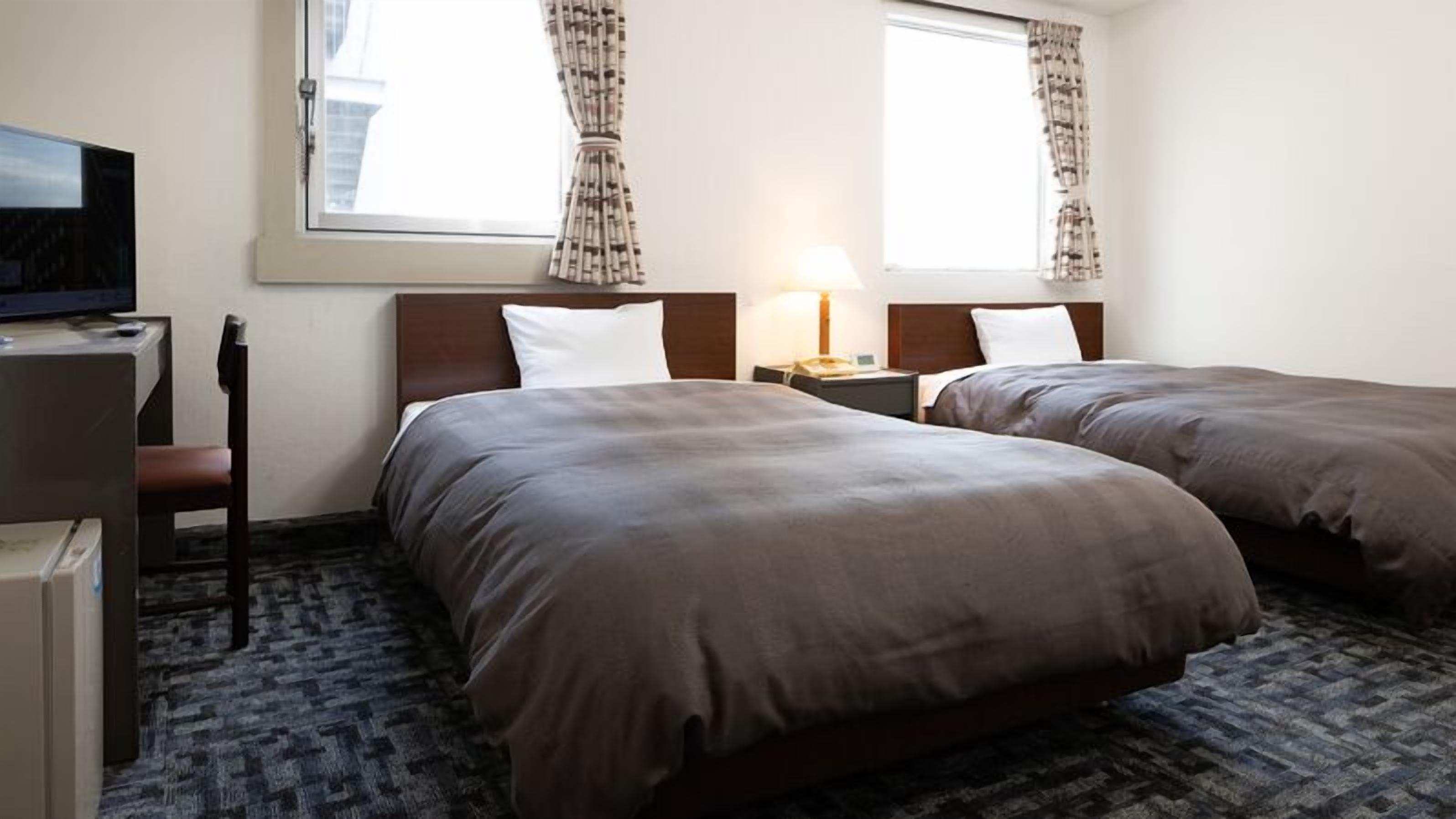 Ett hotellrum med två sängar, ett skrivbord med en dator, en stol och ett fönster med gardiner.