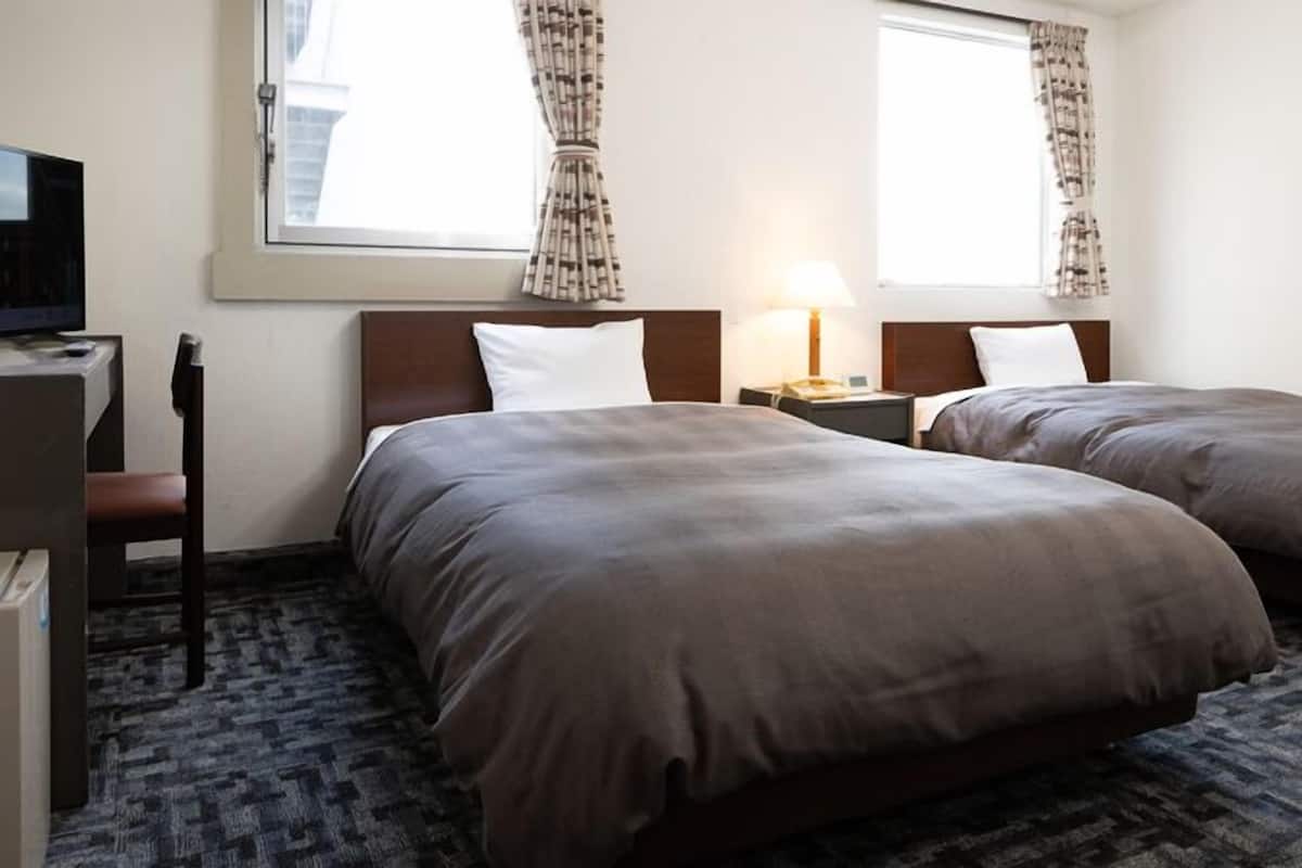 A hotel room with two beds, a desk with a computer, a chair, and a window with curtains.