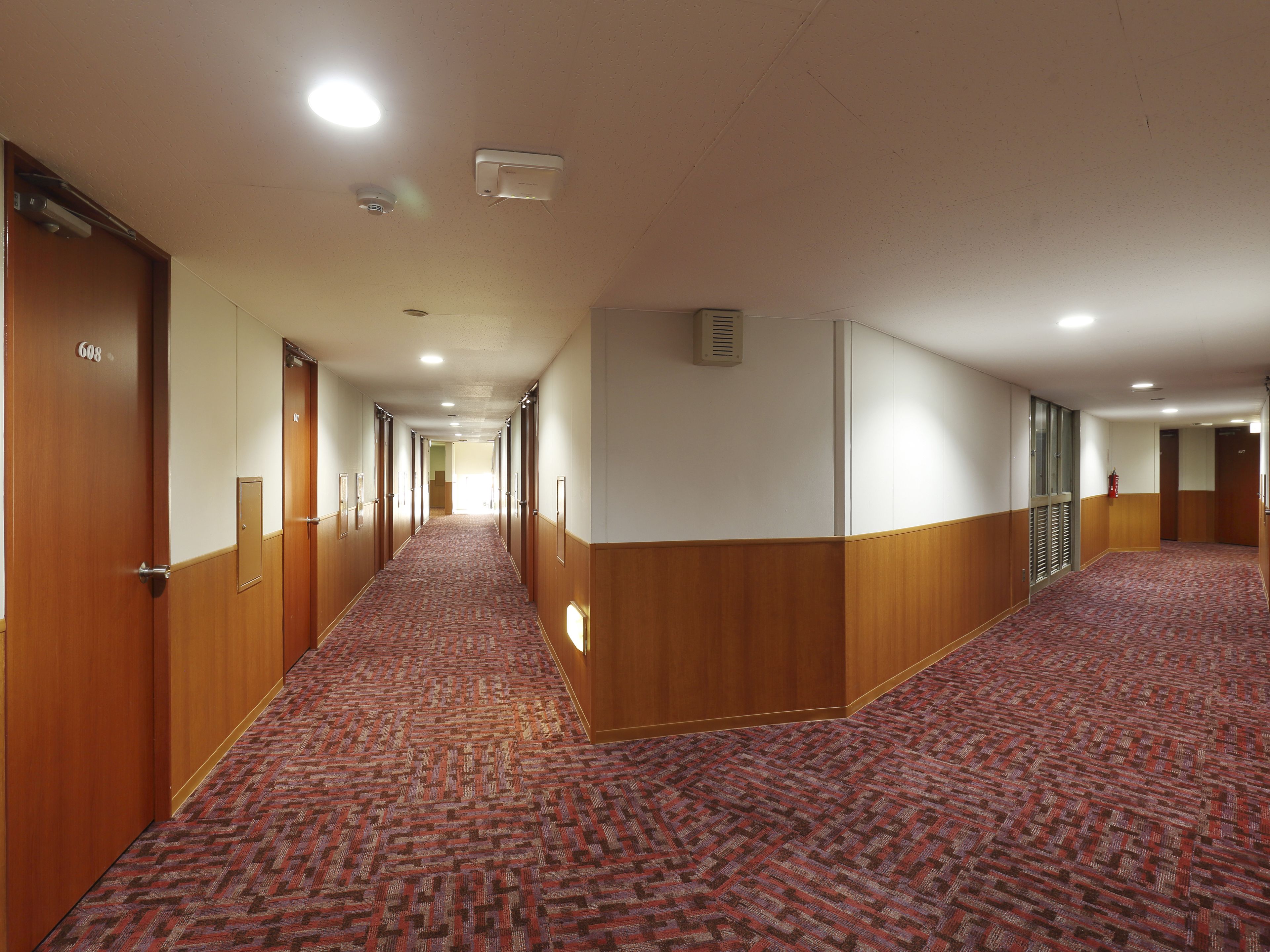 Un pasillo de hotel con puertas de madera, alfombra estampada e iluminación empotrada.
