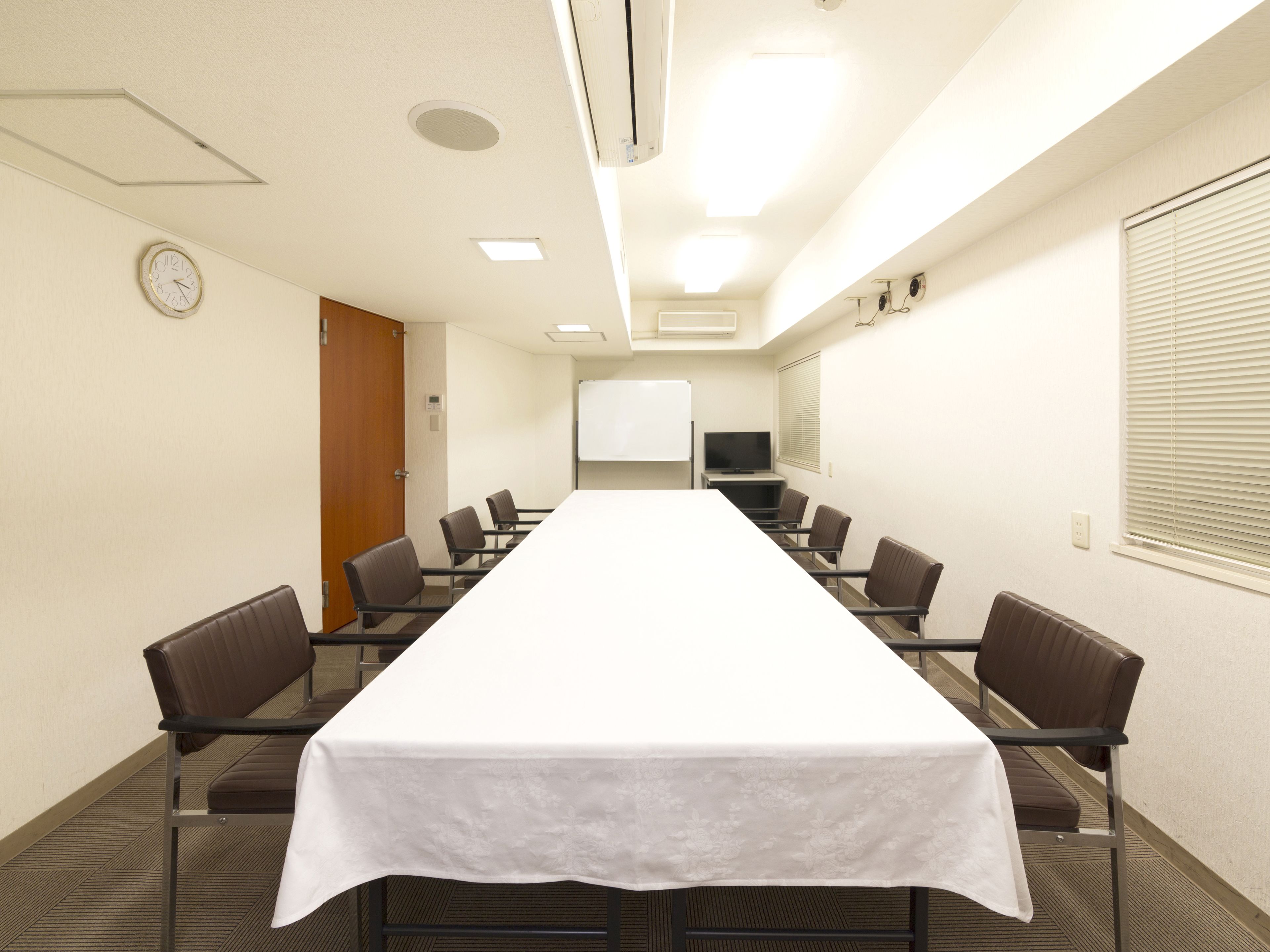 A conference room with a long table, chairs, a clock, a whiteboard, and a TV.