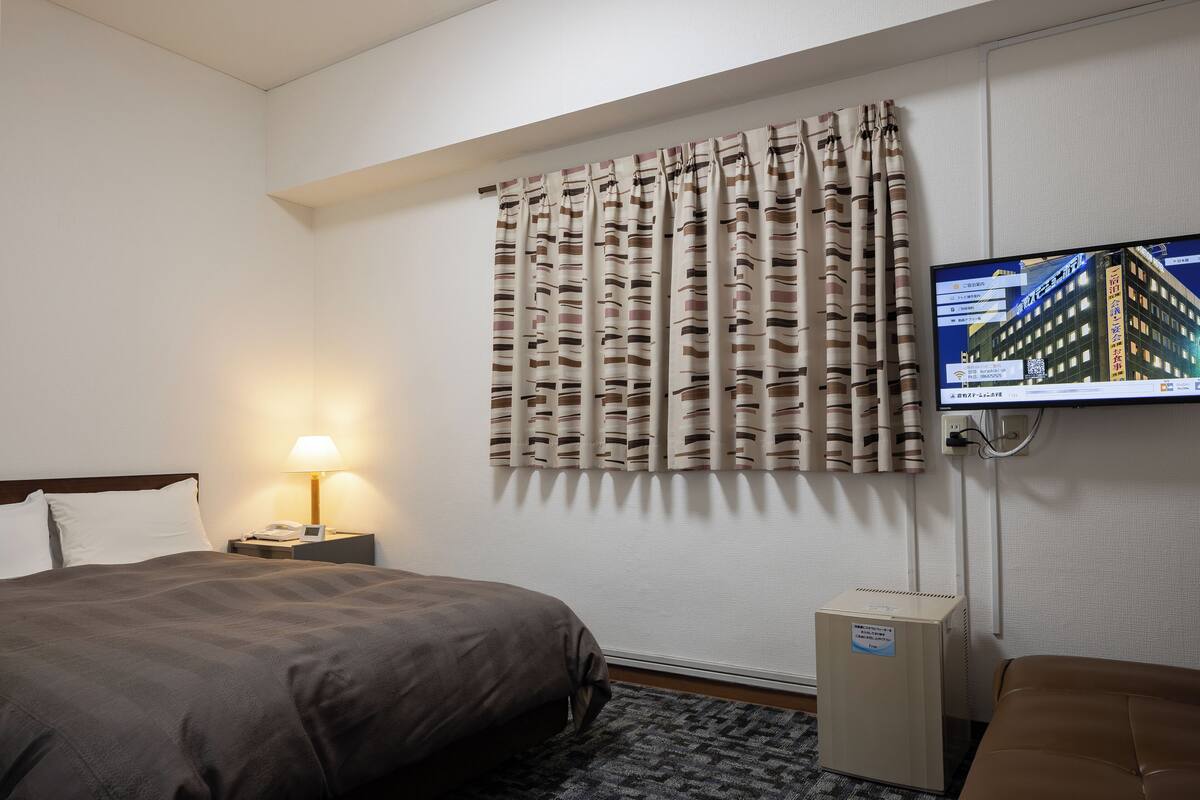 Ein Hotelzimmer mit einem Bett, einem Nachttisch mit Lampe, einem an der Wand befestigten Fernseher und einem kleinen Schrank.
