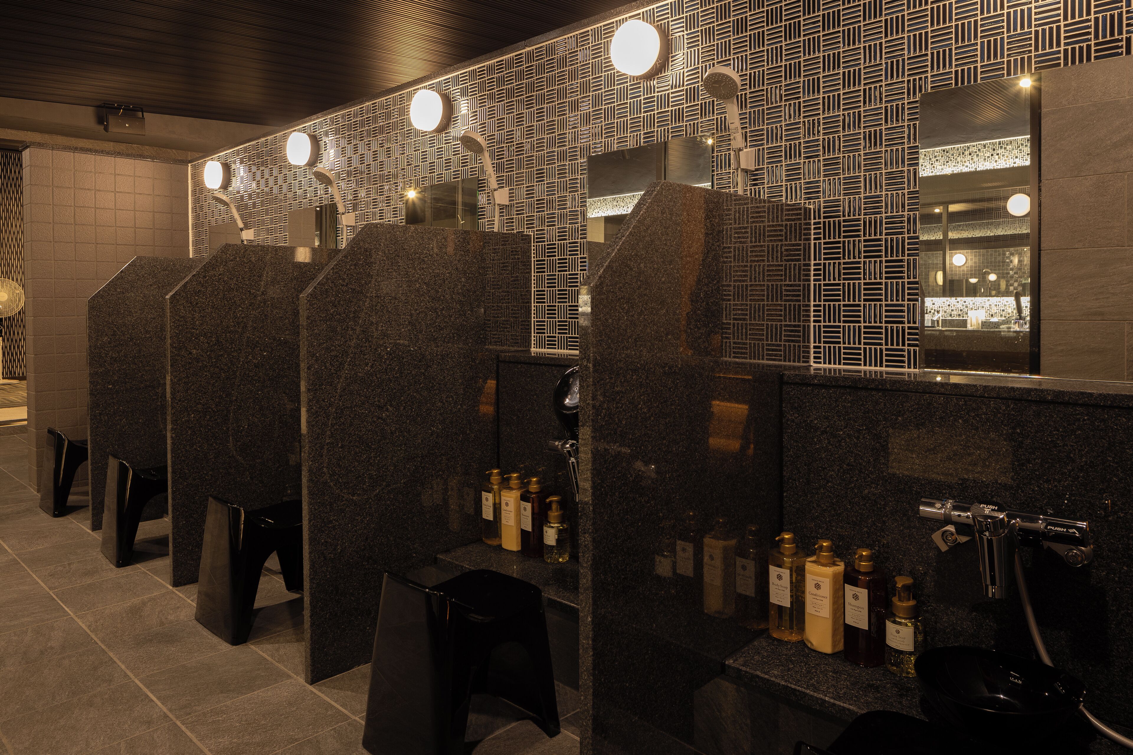 A row of dark granite sinks with mirrors above them, and a tiled wall with a geometric pattern.